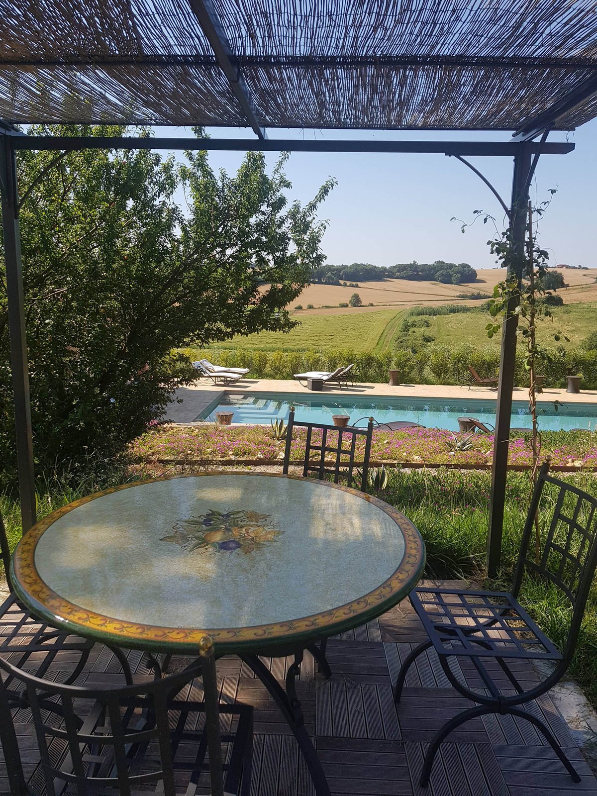 Un tavolo sotto il pergolato, con la piscina sullo sfondo